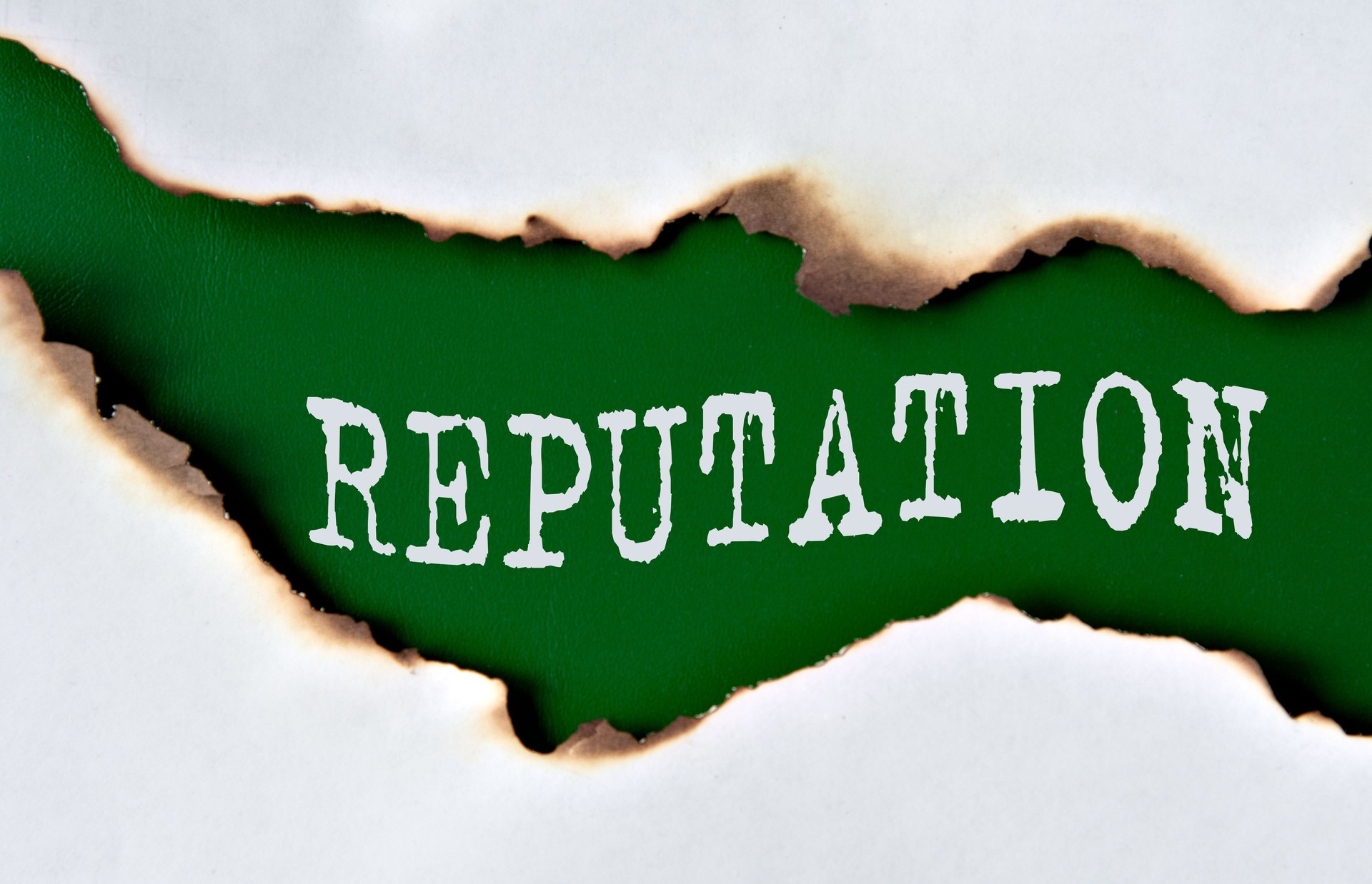 REPUTATION - word on green paper against the background of a sheet of paper damaged by fire